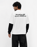 A man shown from the back wearing a white graphic t-shirt with black text, layered over a black long-sleeve shirt, black jeans, and white sneakers, against a plain white studio background.
